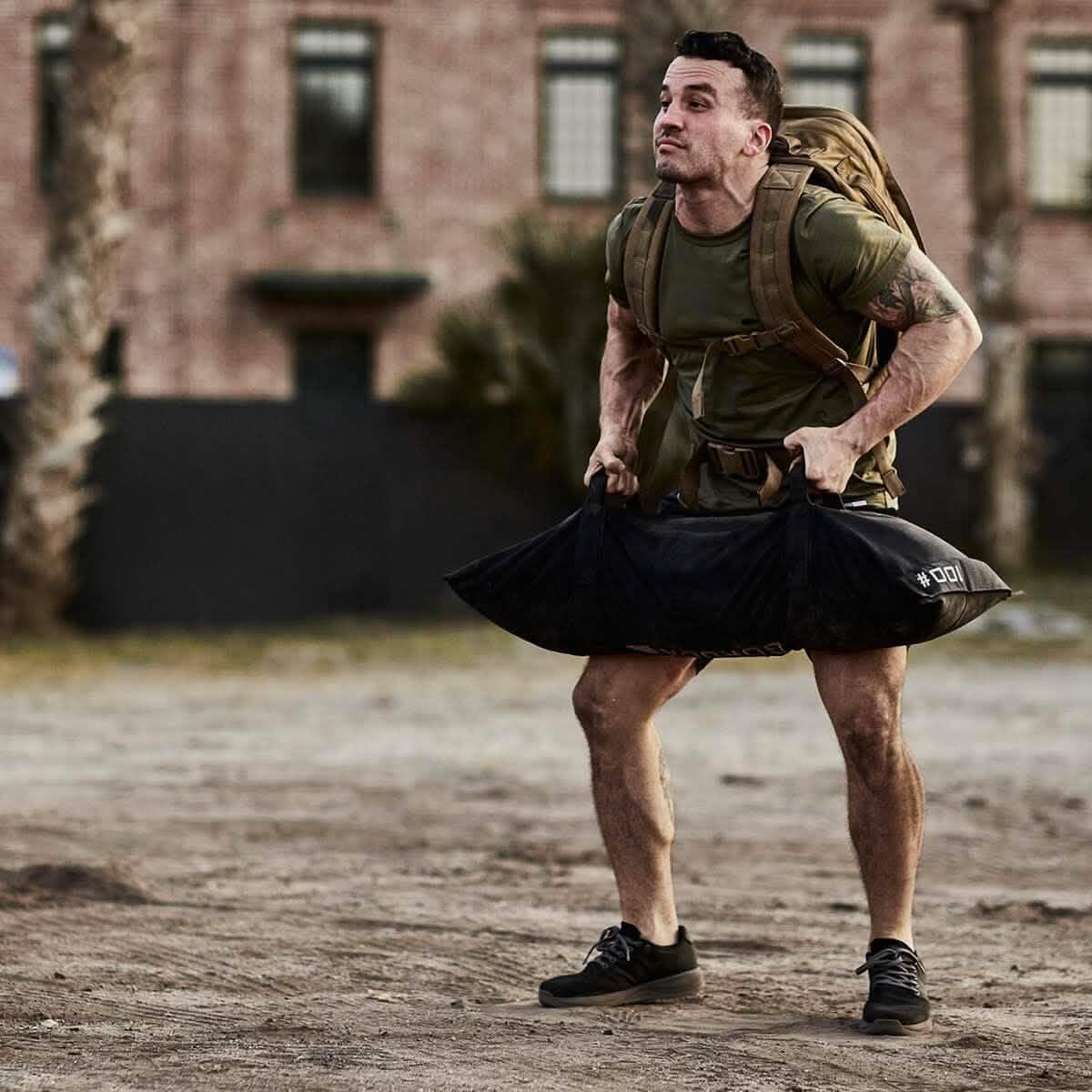 Man rucking outdoors with GORUCK backpack and sandbag, tough fitness gear in urban setting