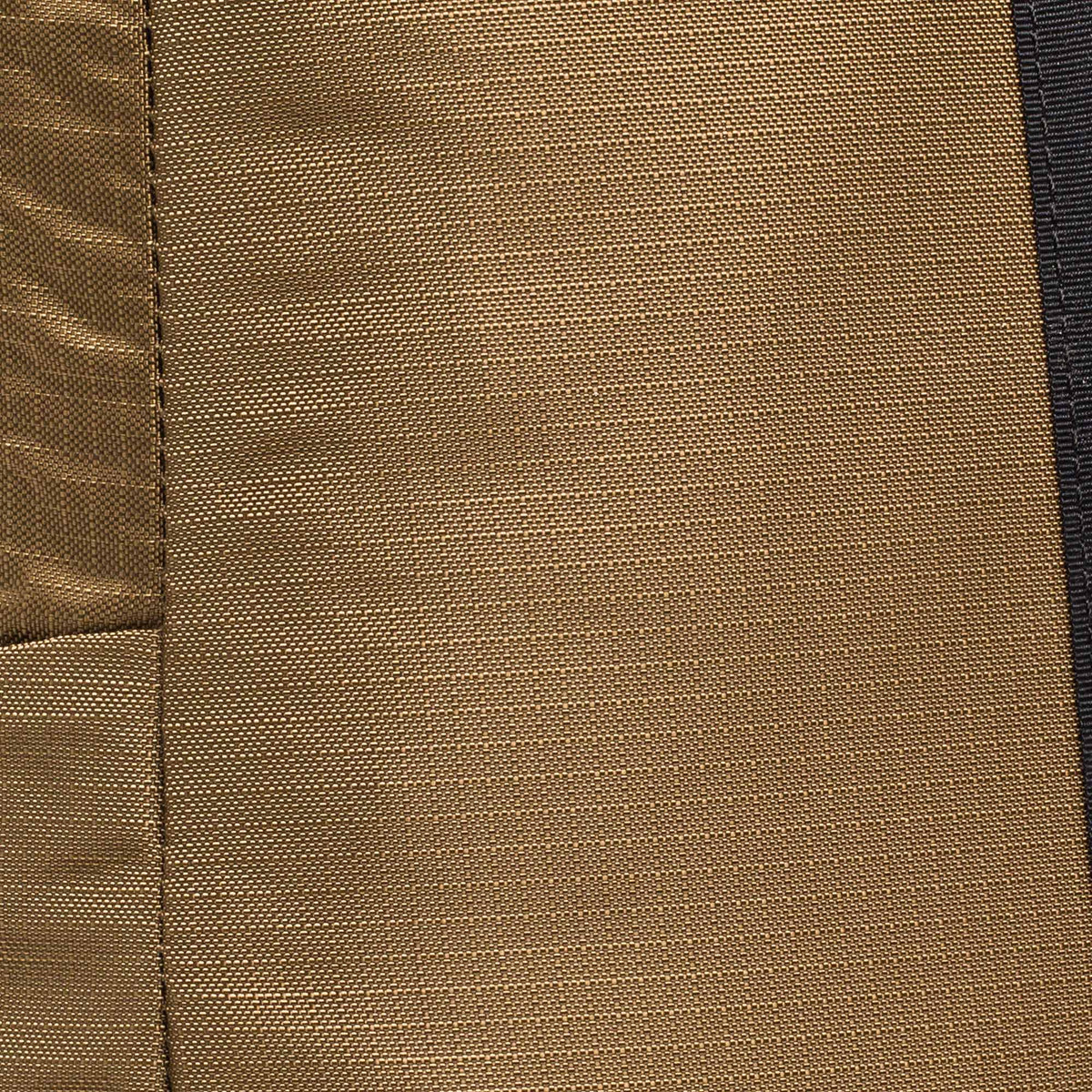 Close-up of brown textured fabric with visible stitching on a Basic Rucker® backpack, featuring a dark vertical strip on the right side.