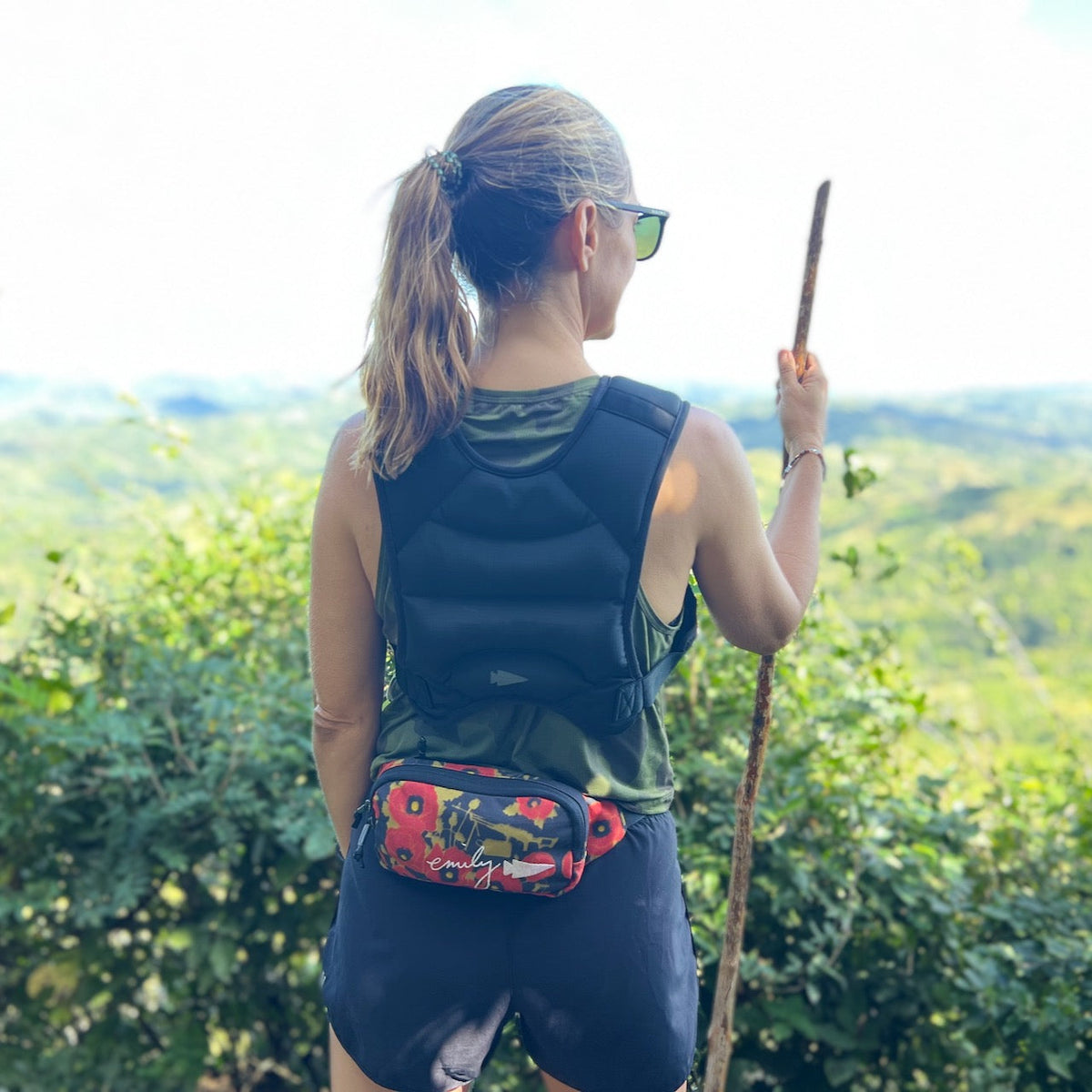 A woman hikes with a stick, overlooking a green landscape while wearing the Spy Ruck Women's Weighted Vest.