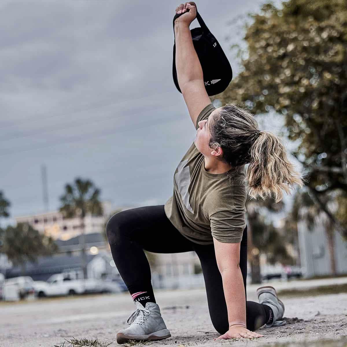 Woman outdoors lifting GORUCK rucksack, wearing athletic gear and rucker boots