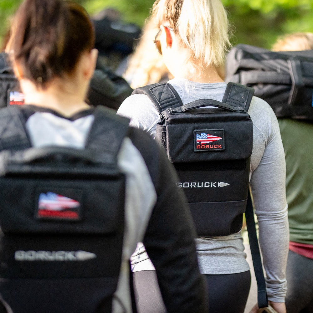 A group enjoys a sunny outdoor stroll wearing Ruck Plate Carrier 3.0 weighted backpacks with lumbar support.