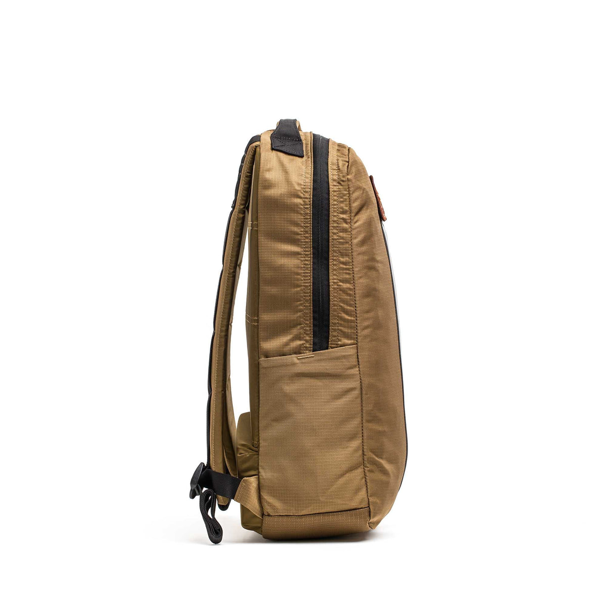 Side view of a tan Basic Rucker® backpack with black zippers and straps, standing upright on a white background.