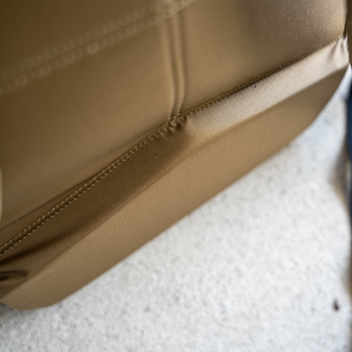 Close-up of a tan Basic Rucker resting on a light-colored, textured surface—ideal for carrying your ruck plate on any rucking adventure.